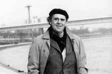 EIn schwarz-weiß-Foto vom Schriftsteller Heinrich Böll, er schaut direkt in die Kamera und geht an einem Fluss entlang.