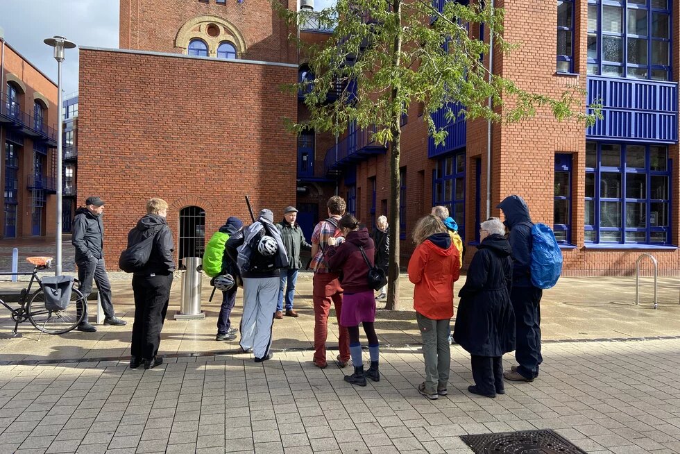 Foto vom Stadtrundgang in Bremerhaven, ca. 15 Personen stehen im Kreis vor einem alten Backsteingebäude der Hochschule Bremerhaven