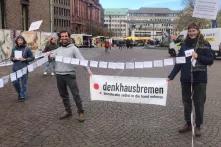 Ein Foto von einer Demonstation: Zwei Menschen halten ein Banner auf dem steht "denkhausbremen", sie lachen dabei.