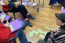 Foto von Menschen, die zusammensitzen und diskutieren. Auf dem Boden zwischen ihnen liegen farbige Karten mit Ideen.