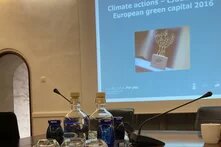 Im Vordergrund sieht man einen Konferenztisch, im Hintergrund eine Powepoint Präsentation zum THema "European green capital 2016"