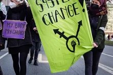 Foto von einer feministischen Demo, auf dem Banner im Vordergrund steht: System Change 