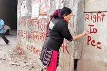 Frau schreibt mit roter Farbe "Right to Pee" an eine Wand in Indien