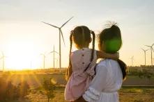 Kind auf dem Arm einer Frau, blicken auf Windmühlen in der Landschaft, am Horizont die untergehende Sonne