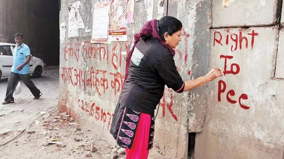 Frau schreibt mit roter Farbe "Right to Pee" an eine Wand in Indien